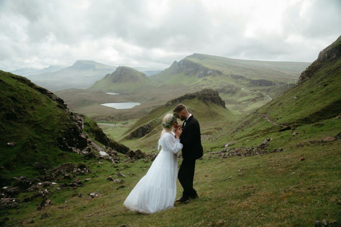 A bride and groom standing on a grassy hill