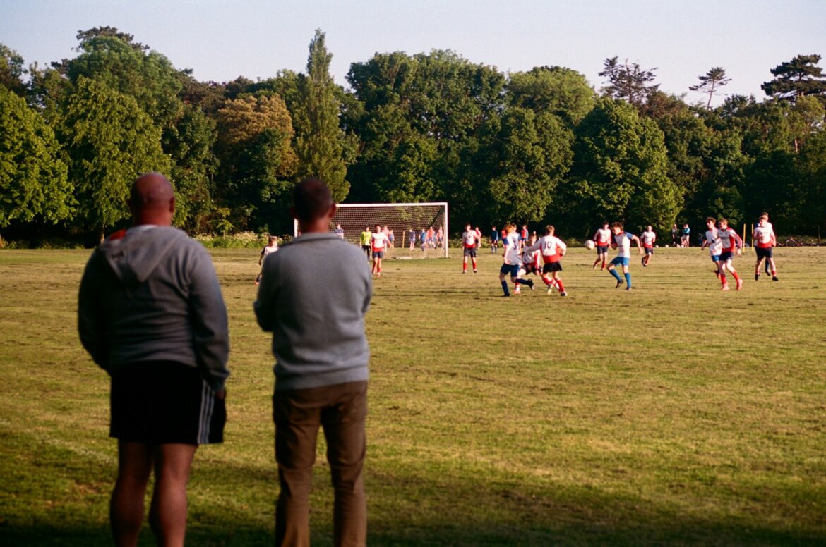 Men watch a soccer game in a park.