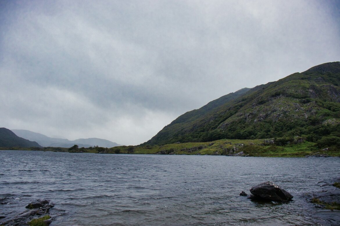 A calm lake with rolling hills under a cloudy sky.