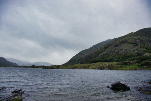 A calm lake with rolling hills under a cloudy sky.