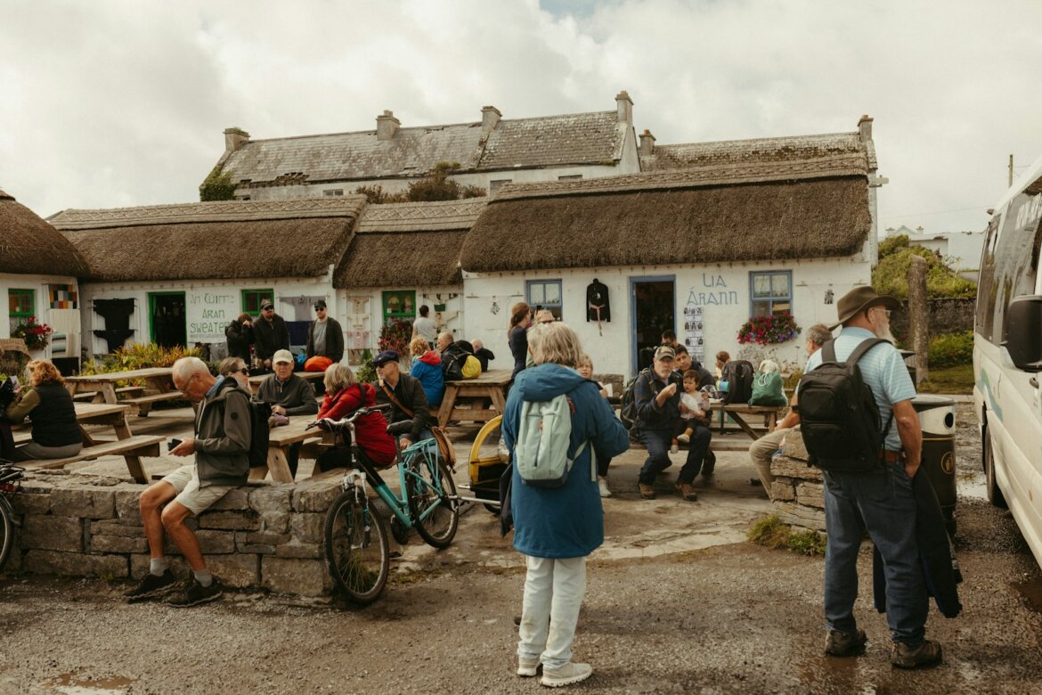 People gathered outside thatched-roof buildings on a cloudy day.