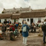 People gathered outside thatched-roof buildings on a cloudy day.