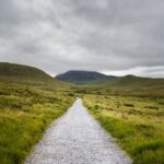Gravel path leads through green hills under cloudy sky