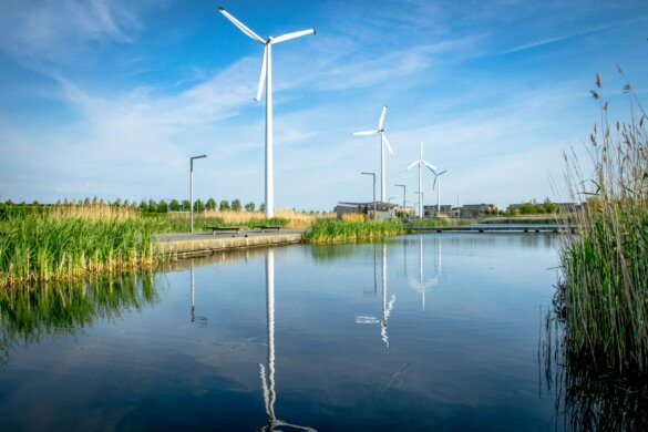 Wind turbines reflected in calm water under blue sky.