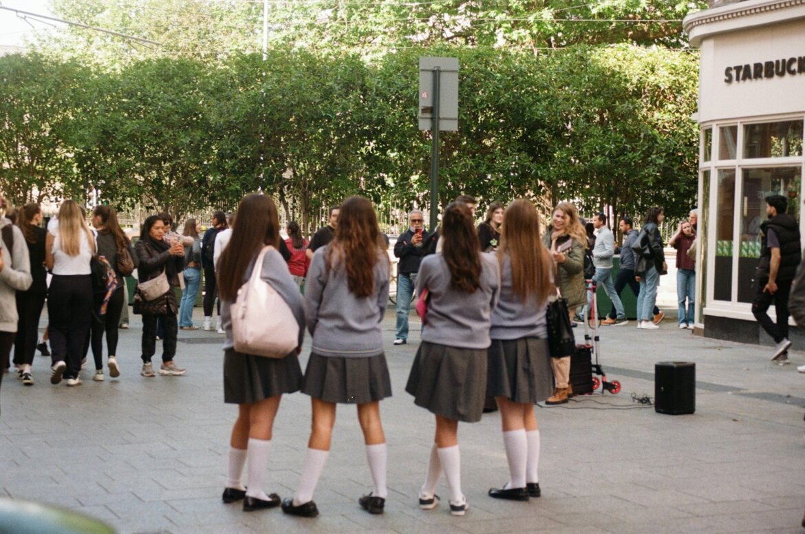 Four girls in school uniforms stand together outside.