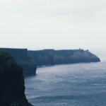 Cliffs meet the sea under a cloudy sky.