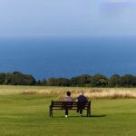 Two people sitting on a bench in a field