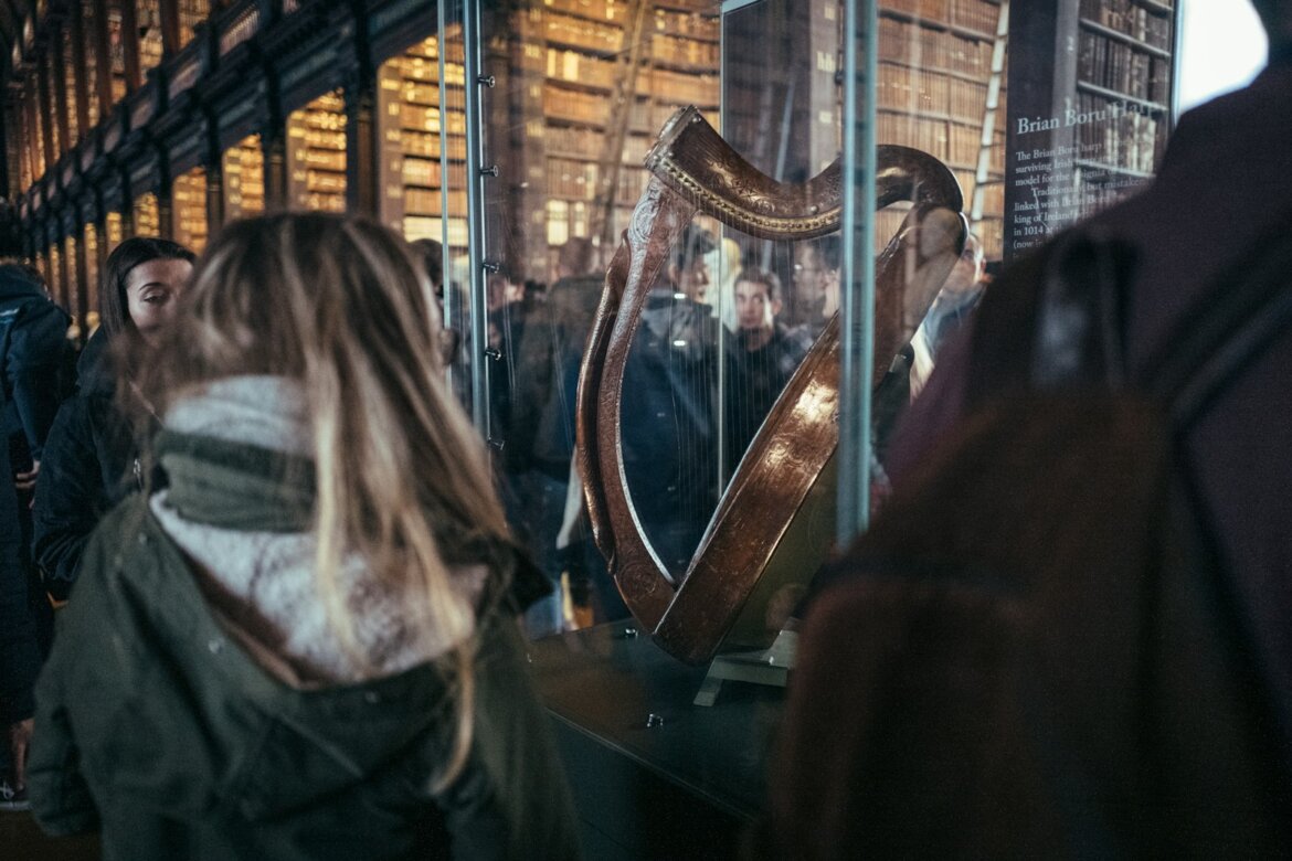People viewing an ornate harp in a library exhibit.