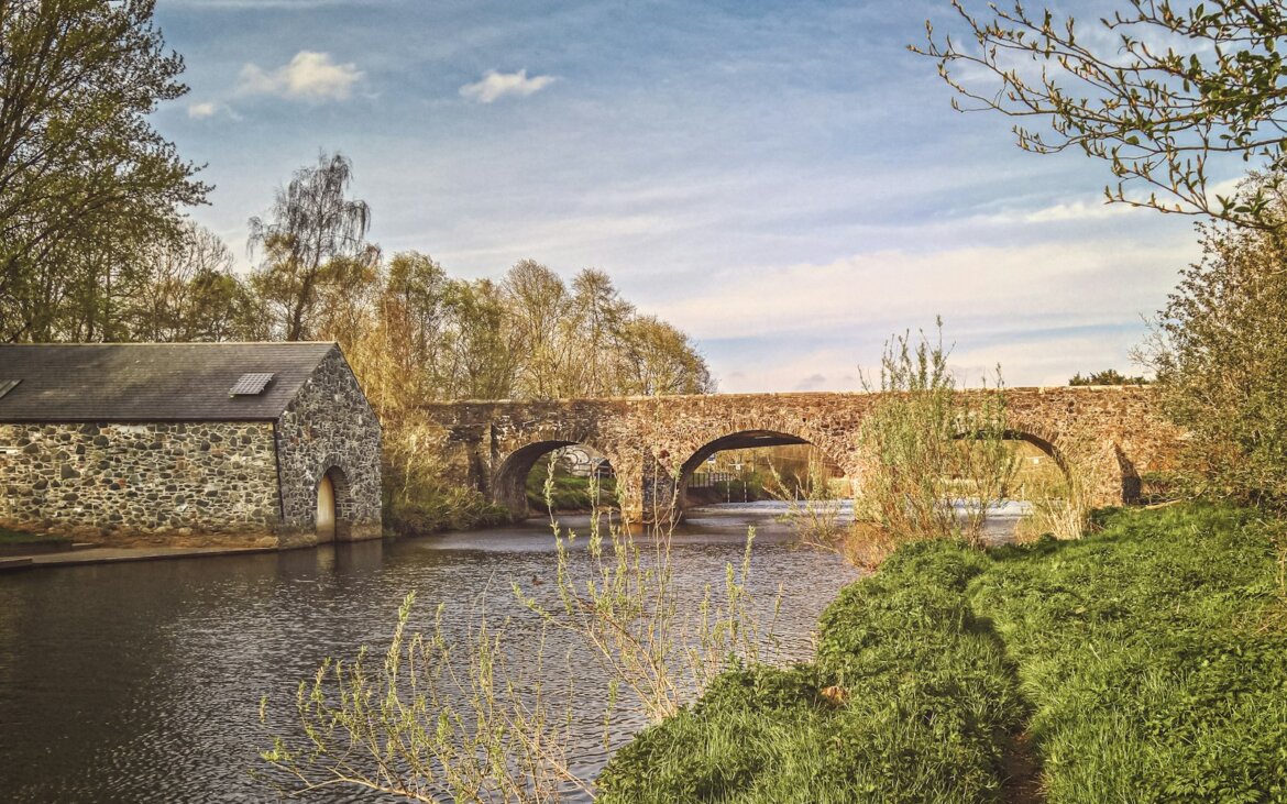 brown concrete bridge over river under white clouds and blue sky during daytime