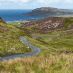 gray asphalt road on green mountain beside body of water during daytime